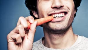 guy smiles while eating carrot