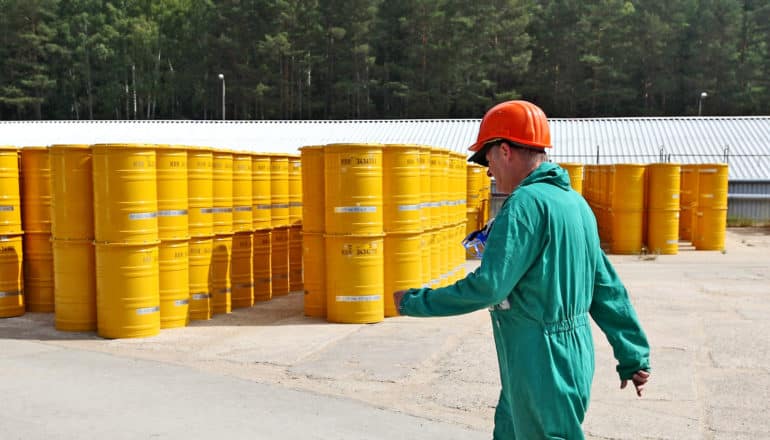 worker walks by nuclear waste barrels