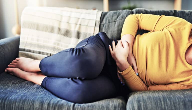 IBD - person holds stomach while lying on couch