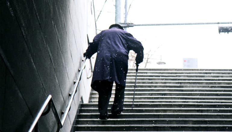 Man walking upstairs with cane (Parkinson's disease concept)