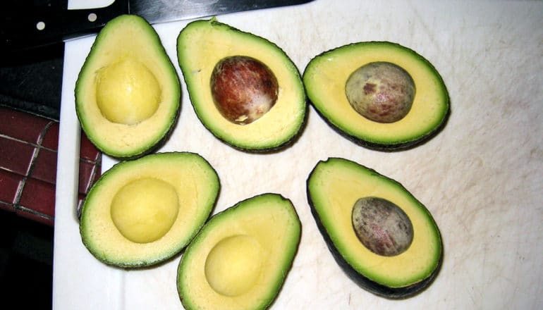 The image shows three avocados cut in half on a white cutting board. (avocado concept)