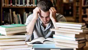 The image shows a stressed college student reading in the library.