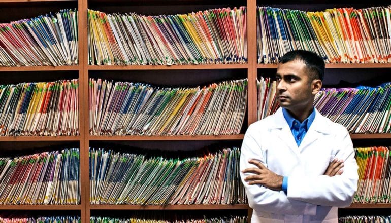 The image shows a doctor with his arms folded in a medical record room. (doctors concept)