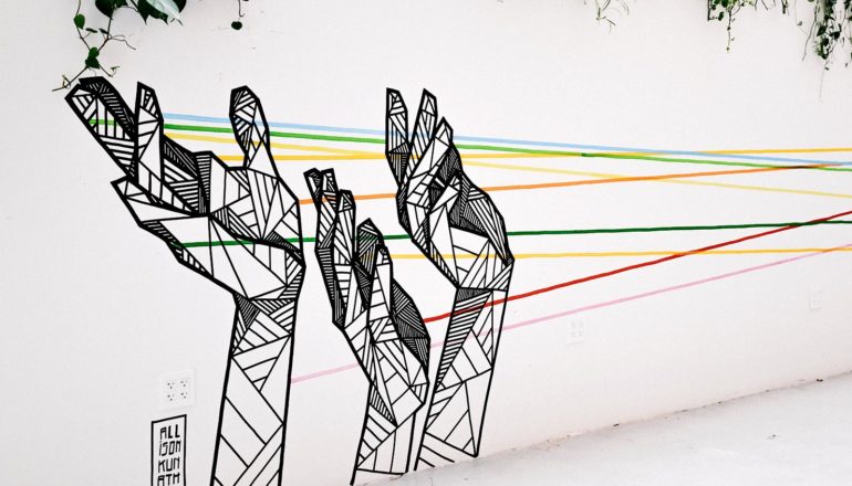 The image shows art on a wall depicting hands with several lines of color coming off them. (CRISPR concept)