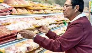 The image shows a man buying chicken at the supermarket. (salmonella concept)