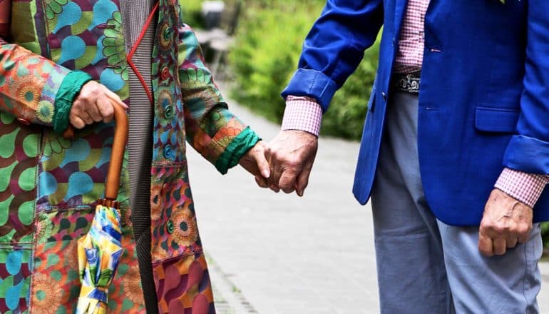 elderly person in colorful coat holds hands with elderly person in blue blazer outdoors