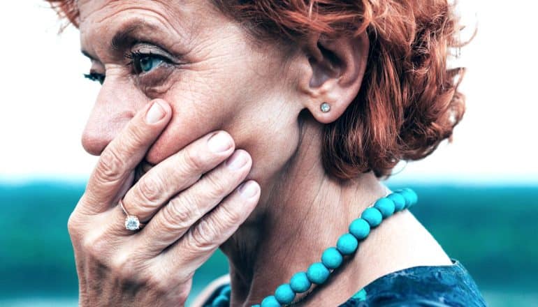 red-headed mid-life woman covers mouth as if in shock - mid-life stress