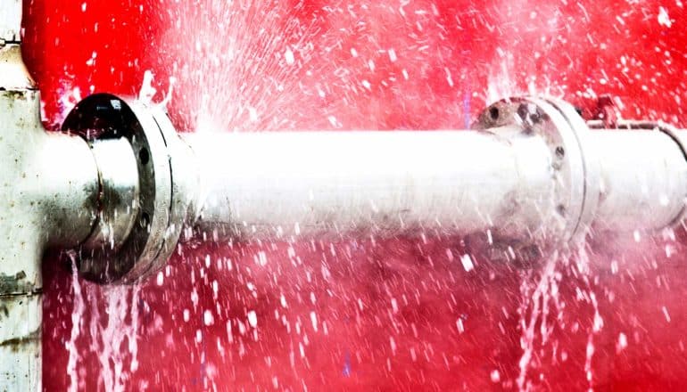 water sprays from metal pipe in front of red wall