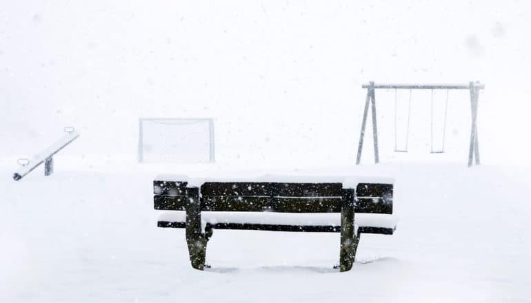 A park bench looks out onto a park covered in snow