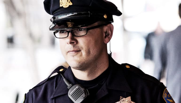 A police officer in uniform wearing glasses looks off camera to his right.