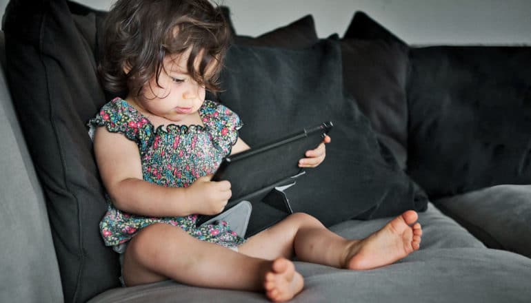 toddler girl uses tablet on black couch