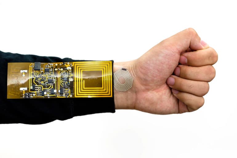 outstretched arm and fist. Golden circuitry on a rectangle forms the receiver on the arm, while a silver pattern on a small circle sits on skin of wrist