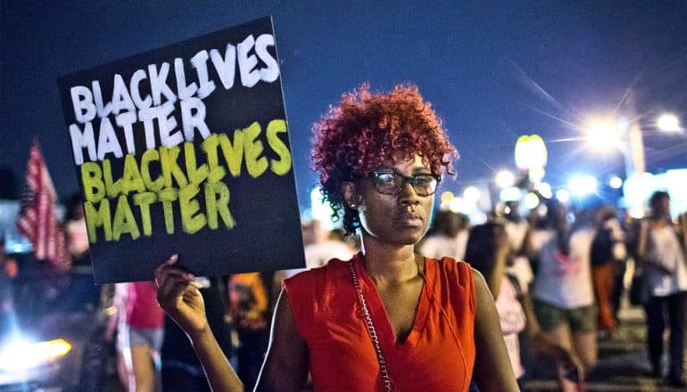 The image shows a protestor holding a Black Lives Matter sign in Ferguson, Missouri.