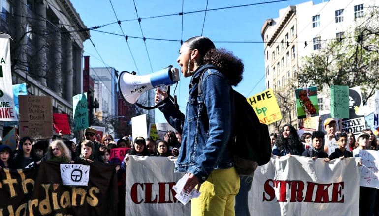 The image shows a young climate activist speaking into a bullhorn at a protest against climate change inaction. (climate change concept)