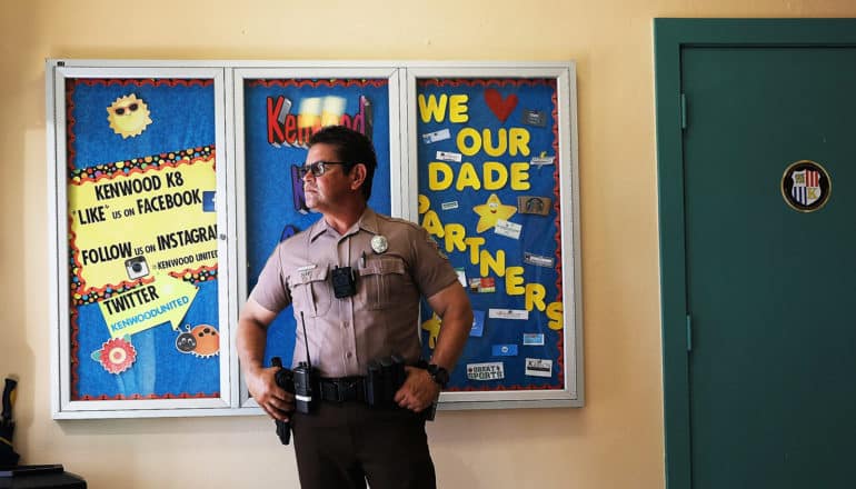 police officer stands in front of school bulletin board