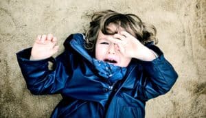 A young child lays in a sand box while crying and wiping away tears