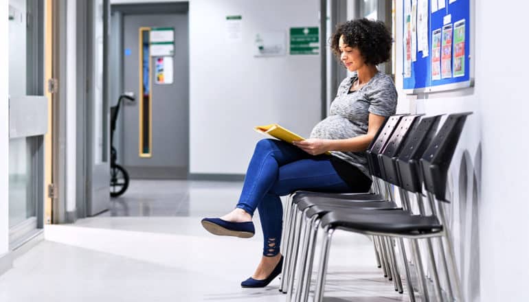 pregnant person sits with magazine in hospital hallway