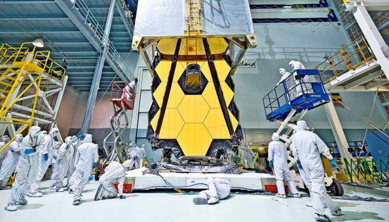 engineers in white suits gather around yellow reflective telescope panel