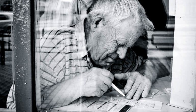 A man leans over a table as he uses a pen to check a lottery ticket