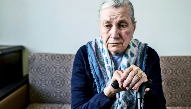 An older woman sits on the couch while holding a cane