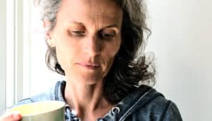 A woman holds a cup of coffee as she looks down with worry