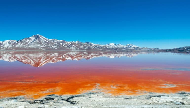 gray mountains behind bright orange shallow water