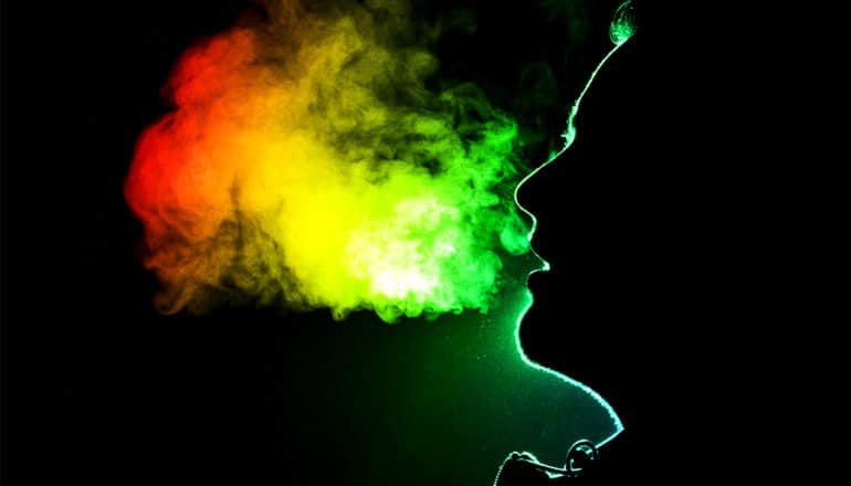 A person exhales and their breath is lighted from behind with green, yellow, and orange