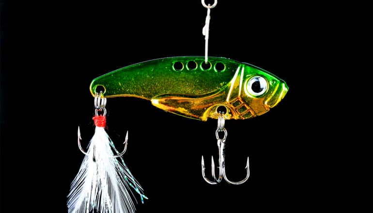 A bright green fish lure with a white feather tail and two sets of hooks hangs against a black background