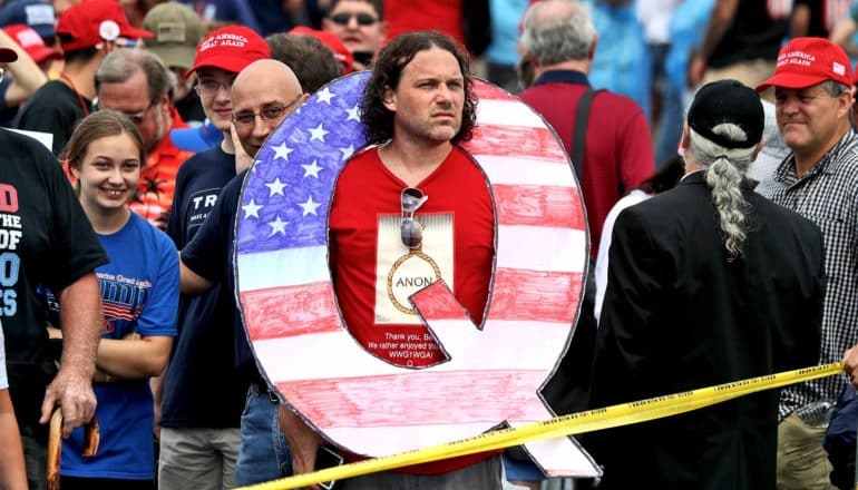 man with large US-flag colored Q around his neck in crowd