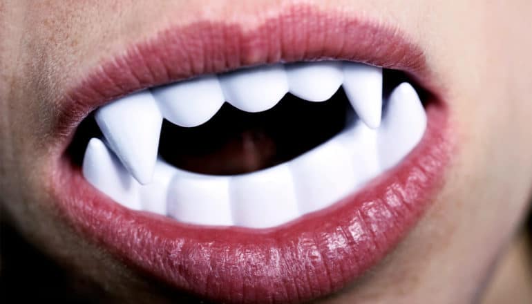 A person has fake vampire teeth in their mouth