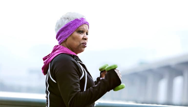 A woman walks outside with weights while wearing a purple headband and workout clothes