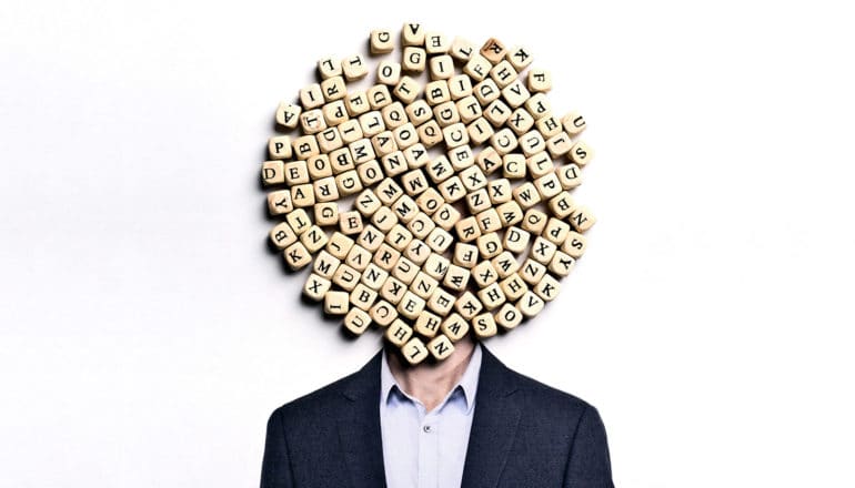 A man in a suit has letter tiles covering his face