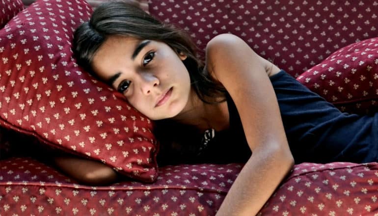 A teen looks tired laying down on a red couch