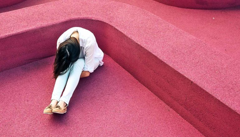 A woman has her head on her knees while sitting on the ground in a red structure