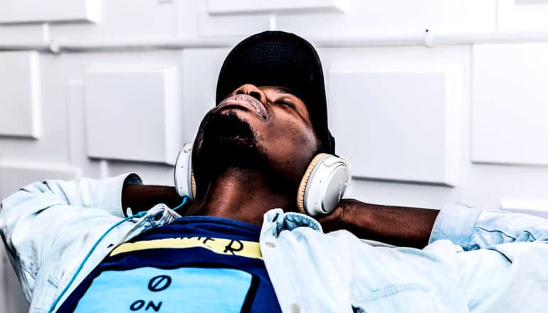 A man leans back on his hands as he's listening to music through headphones