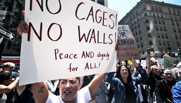 A woman holds a sign that reads "No cages! No walls! Peace and equality for all!" during a protest