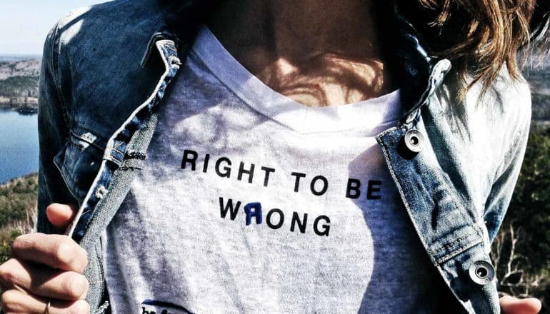 A person pulls their jean jacket to show their shirt, which reads "Right to be wrong" with the "r" in "wrong" backward