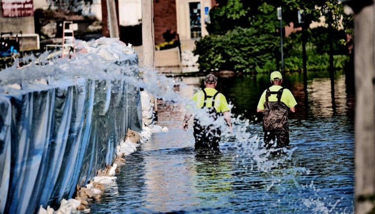 Two workers walk through knee high flood water as more pours over a makeshift barricade