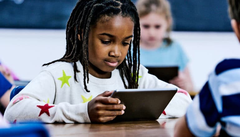 A young student holds a tablet in the classroom