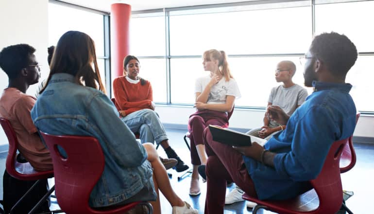 people sit in circle, one of whom has sad expression