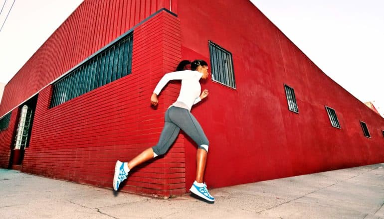 A woman runs around the corner of a red building