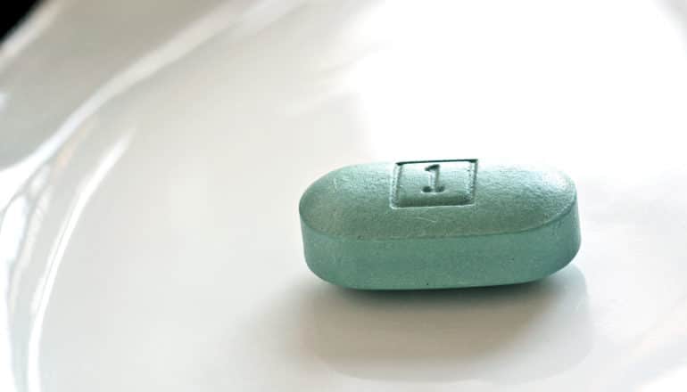 A single green/blue HAART pill sits on a white dish