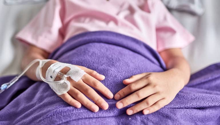 mid-view of a child in bed with IV in hand