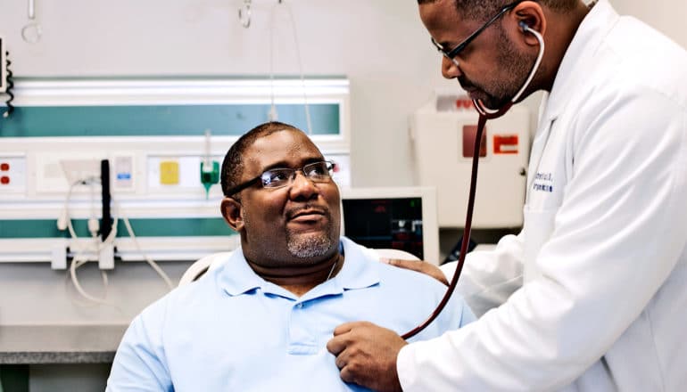 A doctor checks a man's heartbeat with a stethoscope