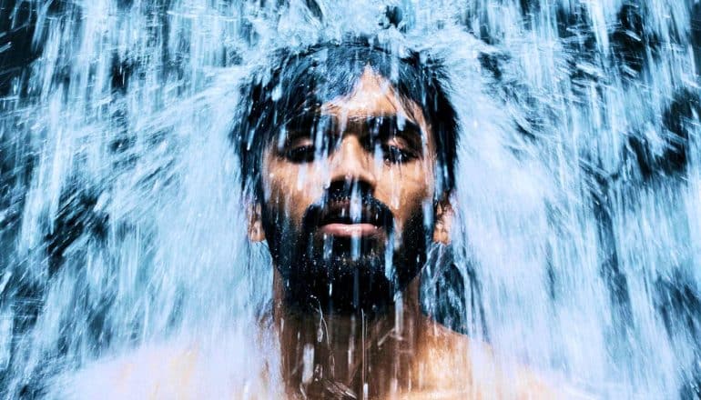 A man closes his eyes as a waterfall pours down on his head