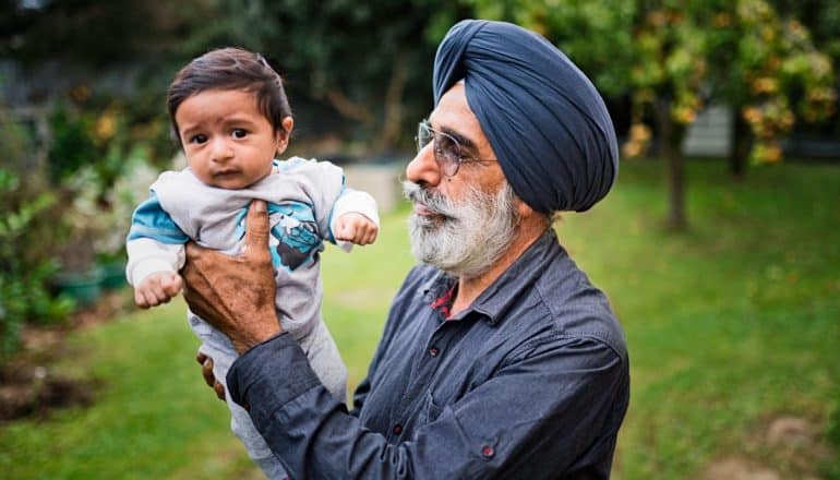 older Sikh man holds up baby outdoors