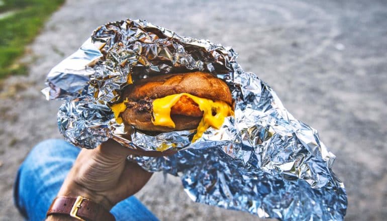 hand holds cheesy sandwich in tin foil