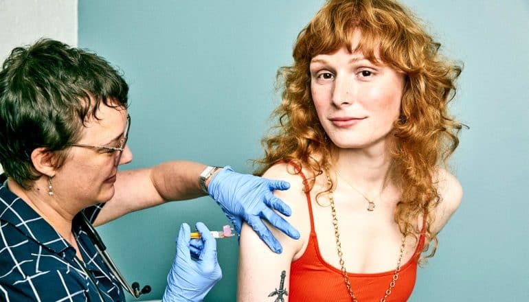 A doctor gives a woman with red hair in a red top a flu shot