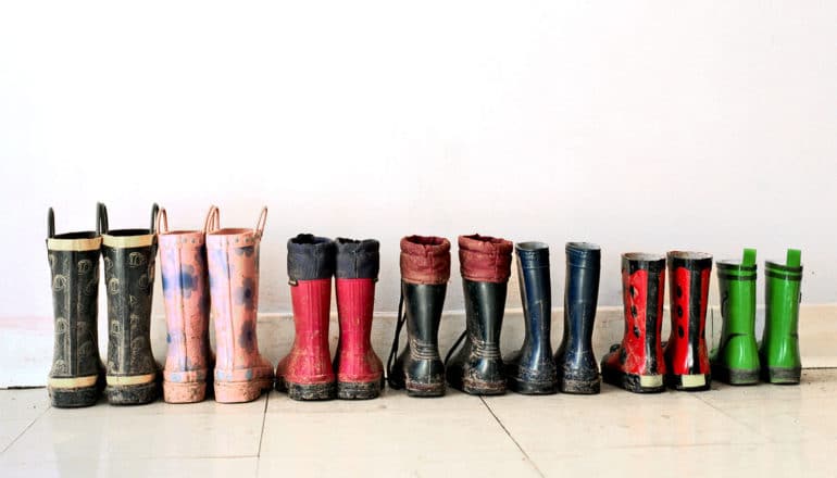 A row of smaller and smaller children's rain boots sit against a wall