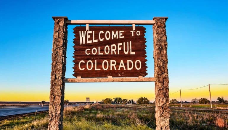 A sign reads "Welcome to colorful Colorado" on the side of a road with the sun rising in the background